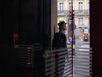 Movie still from “First Name: Carmen” (1983), directed by Jean-Luc Godard – A man standing in front of a building with traffic lights; Wide shot, Low angle