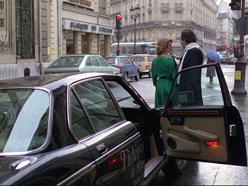 Movie still from “First Name: Carmen” (1983), directed by Jean-Luc Godard – A couple of people standing next to a black car; Wide shot, Over the shoulder angle