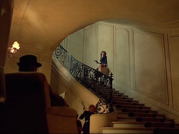 Movie still from “First Name: Carmen” (1983), directed by Jean-Luc Godard – A woman walking down a staircase in a room; Wide shot, Low angle