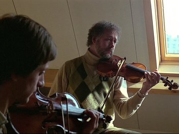 Movie still from “First Name: Carmen” (1983), directed by Jean-Luc Godard – A man playing a violin while another man looks on; Close Up shot, Low angle
