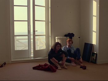 Movie still from “First Name: Carmen” (1983), directed by Jean-Luc Godard – A couple of people sitting on the ground in a room; Wide shot, High angle
