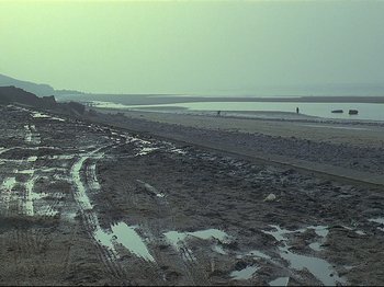 Movie still from “First Name: Carmen” (1983), directed by Jean-Luc Godard – A beach with a person walking on the beach in the background; Extreme Wide shot, High angle