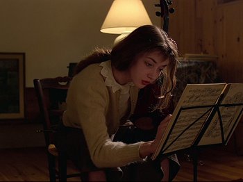 Movie still from “First Name: Carmen” (1983), directed by Jean-Luc Godard – A woman sitting in a chair looking at a sheet of music; Medium shot, Over the shoulder angle