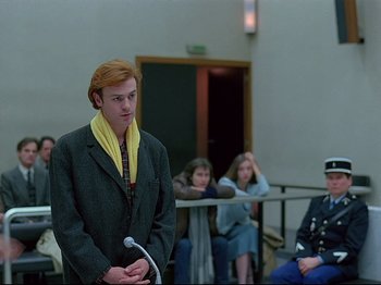 Movie still from “First Name: Carmen” (1983), directed by Jean-Luc Godard – A man standing in front of a group of people; Medium shot, Low angle