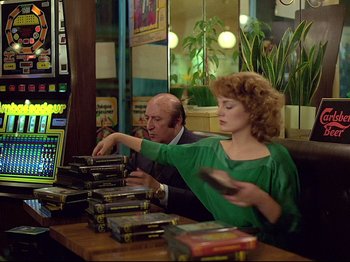 Movie still from “First Name: Carmen” (1983), directed by Jean-Luc Godard – A man and a woman sitting in front of stacks of books; Medium shot, Over the shoulder angle