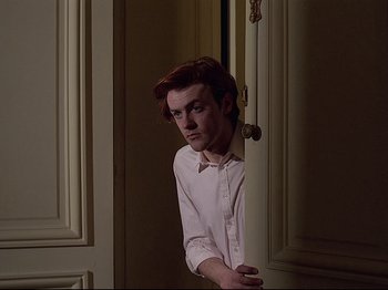 Movie still from “First Name: Carmen” (1983), directed by Jean-Luc Godard – A man leaning against a wall in a room; Medium shot, Over the shoulder angle