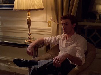 Movie still from “First Name: Carmen” (1983), directed by Jean-Luc Godard – A man sitting in a chair in front of a lamp; Medium shot, Low angle