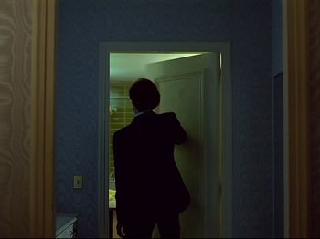 Movie still from “First Name: Carmen” (1983), directed by Jean-Luc Godard – A man standing in a doorway in the dark; Wide shot, Over the shoulder angle