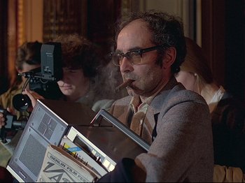 Movie still from “First Name: Carmen” (1983), directed by Jean-Luc Godard – A man smoking a cigar while sitting in a chair; Medium shot, Low angle
