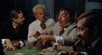 Movie still from “Fitzcarraldo” (1982), directed by Werner Herzog – Two men sitting at a table and one of the men is holding a glass of wine; Medium shot, Over the shoulder angle