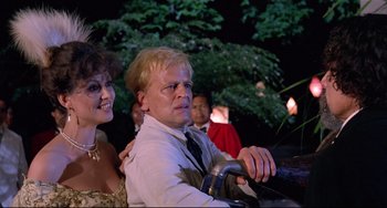 Movie still from “Fitzcarraldo” (1982), directed by Werner Herzog – A man and a woman sitting next to each other in front of trees; Close Up shot, Low angle