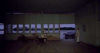 Movie still from “Fitzcarraldo” (1982), directed by Werner Herzog – A man sitting at a table in front of a large body of water; Extreme Wide shot, High angle