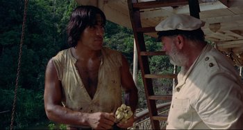 Movie still from “Fitzcarraldo” (1982), directed by Werner Herzog – A man is holding a banana while talking to another man; Medium shot, Low angle