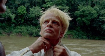 Movie still from “Fitzcarraldo” (1982), directed by Werner Herzog – A man with blonde hair and a white shirt is standing in a river; Close Up shot, Low angle