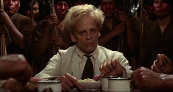 Movie still from “Fitzcarraldo” (1982), directed by Werner Herzog – A man sitting at a dinner table with a plate of food; Close Up shot, Low angle