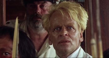 Movie still from “Fitzcarraldo” (1982), directed by Werner Herzog – A man with blonde hair is looking at the camera while another man looks on; Close Up shot, Low angle