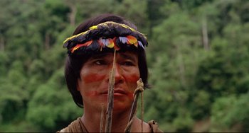 Movie still from “Fitzcarraldo” (1982), directed by Werner Herzog – A man with feathers on his head is holding a spear; Close Up shot, Low angle