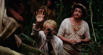Movie still from “Fitzcarraldo” (1982), directed by Werner Herzog – A man with a camera in the woods waving; Medium shot, Over the shoulder angle
