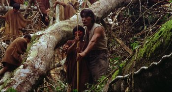 Movie still from “Fitzcarraldo” (1982), directed by Werner Herzog – A man holding a spear while standing next to a tree; Wide shot, Low angle