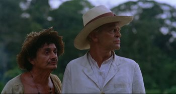 Movie still from “Fitzcarraldo” (1982), directed by Werner Herzog – A man in a hat and a man in a white jacket; Medium shot, Low angle