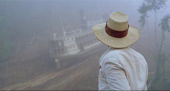Movie still from “Fitzcarraldo” (1982), directed by Werner Herzog – A person wearing a hat looking at a boat in the water; Close Up shot, Low angle