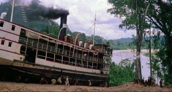 Movie still from “Fitzcarraldo” (1982), directed by Werner Herzog – A large boat is sitting in the sand near a body of water; Extreme Wide shot, Low angle