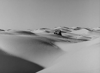 Movie still from “Five Graves to Cairo” (1943), directed by Billy Wilder – A truck driving through the sand dunes in black and white; Extreme Wide shot, High angle