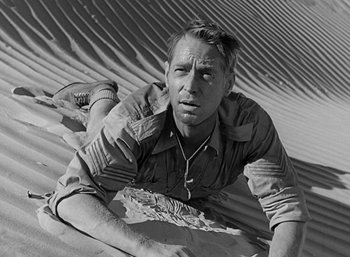 Movie still from “Five Graves to Cairo” (1943), directed by Billy Wilder – A black and white photo of a man laying in the sand; Medium shot, High angle