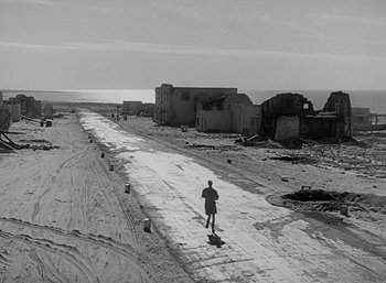 Movie still from “Five Graves to Cairo” (1943), directed by Billy Wilder – A man walking down a dirt road in the middle of the desert; Extreme Wide shot, High angle