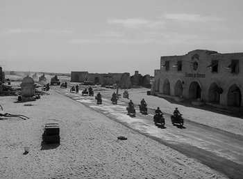 Movie still from “Five Graves to Cairo” (1943), directed by Billy Wilder – A black and white photo of motorcycles driving down a street; Extreme Wide shot, High angle