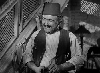 Movie still from “Five Graves to Cairo” (1943), directed by Billy Wilder – An older man wearing a fez and holding a pipe; Medium shot, Low angle