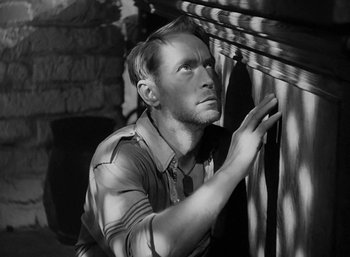 Movie still from “Five Graves to Cairo” (1943), directed by Billy Wilder – A black and white photo of a man leaning against a wall; Close Up shot, High angle