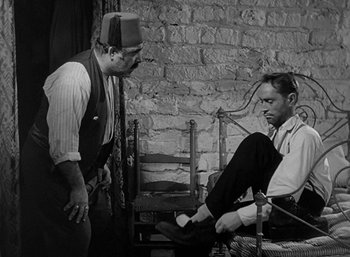 Movie still from “Five Graves to Cairo” (1943), directed by Billy Wilder – Two men are sitting on a chair and one of them has a hat on his head; Medium shot, High angle