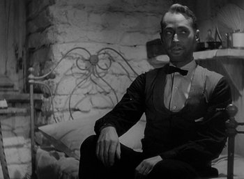 Movie still from “Five Graves to Cairo” (1943), directed by Billy Wilder – A man sitting in front of a brick wall; Medium shot, Low angle