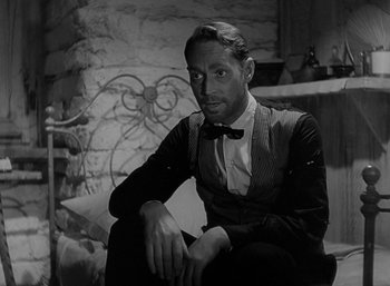 Movie still from “Five Graves to Cairo” (1943), directed by Billy Wilder – A black and white photo of a man sitting on a chair; Close Up shot, Low angle