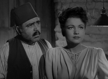 Movie still from “Five Graves to Cairo” (1943), directed by Billy Wilder – An older man and a young woman standing next to each other in front of a brick wall; Medium shot, Over the shoulder angle