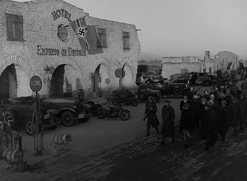 Movie still from “Five Graves to Cairo” (1943), directed by Billy Wilder – A group of people standing in front of a building; Wide shot, High angle