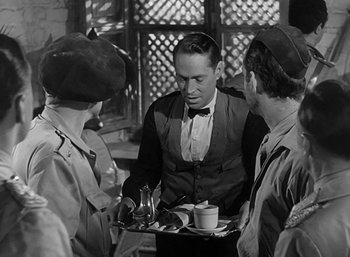 Movie still from “Five Graves to Cairo” (1943), directed by Billy Wilder – A man serving a tray of food to three other people; Medium shot, Over the shoulder angle