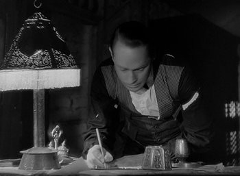 Movie still from “Five Graves to Cairo” (1943), directed by Billy Wilder – A man writing on a piece of paper on top of a table; Medium shot, Low angle