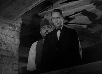 Movie still from “Five Graves to Cairo” (1943), directed by Billy Wilder – A man and a man standing next to each other in a room; Medium shot, Low angle