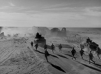 Movie still from “Five Graves to Cairo” (1943), directed by Billy Wilder – A black and white photo of a group of men running across a dirt road; Extreme Wide shot, High angle