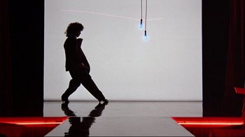 Movie still from “Flashdance” (1983), directed by Adrian Lyne – A person walking on a runway in front of a white wall; Wide shot, Low angle
