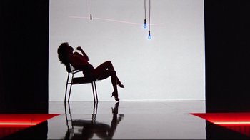 Movie still from “Flashdance” (1983), directed by Adrian Lyne – A woman sitting on a chair in front of lights; Wide shot, Low angle