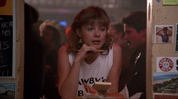 Movie still from “Flashdance” (1983), directed by Adrian Lyne – A woman sitting at a table with a sandwich in front of her face; Close Up shot, Over the shoulder angle