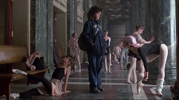 Movie still from “Flashdance” (1983), directed by Adrian Lyne – A group of people in a hallway with a woman in a blue jacket; Wide shot, Over the shoulder angle