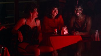 Movie still from “Flashdance” (1983), directed by Adrian Lyne – A group of women sitting at a table in a room; Medium shot, Over the shoulder angle