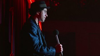 Movie still from “Flashdance” (1983), directed by Adrian Lyne – A man holding a microphone and wearing a hat; Medium shot, Over the shoulder angle