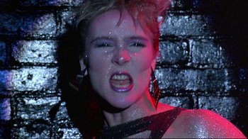 Movie still from “Flashdance” (1983), directed by Adrian Lyne – A woman with her mouth wide open in front of a brick wall; Close Up shot, Low angle