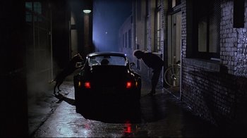 Movie still from “Flashdance” (1983), directed by Adrian Lyne – A man standing next to a car in a dark alley; Wide shot, High angle
