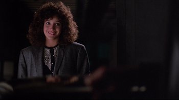 Movie still from “Flashdance” (1983), directed by Adrian Lyne – A woman with curly hair is smiling for the camera; Close Up shot, Over the shoulder angle